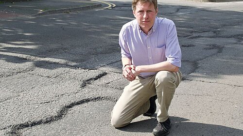 James MacCleary on one knee at the side of a pothole about five feet wide.