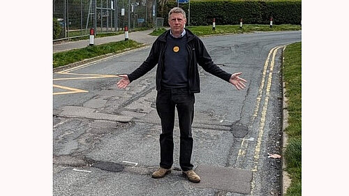 James MacCleary, both hands outstretched, pointing at the many potholes left unfilled in Oakleaf Drive