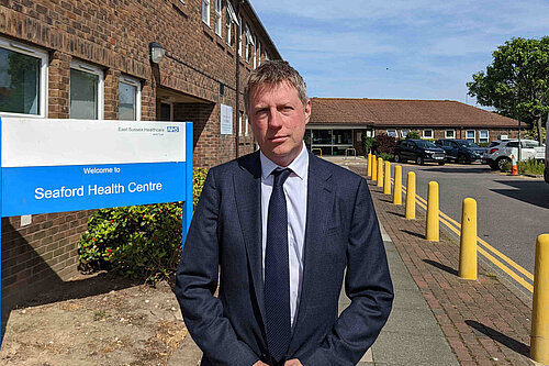 James MacCleary in suit and tie outside a brick building that houses Seaford Health Centre