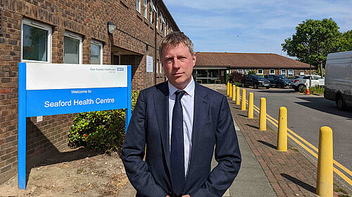 James MacCleary in suit and tie outside a brick building that houses Seaford Health Centre