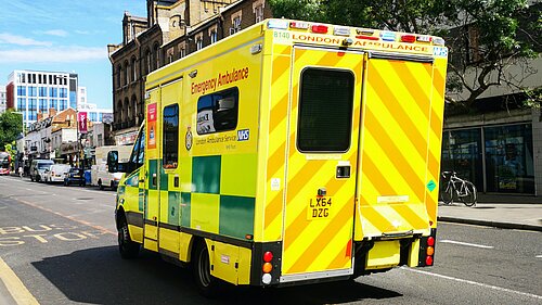 A street scene with a London ambulance in the foreground, taken from the rear.