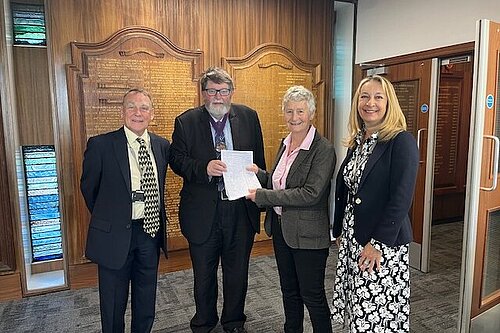 Councillor Sarah Osborne and residents hand their petition to the chair of East Sussex County Council in front of an ornately carved honours list.