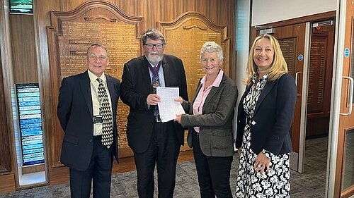 Councillor Sarah Osborne and residents hand their petition to the chair of East Sussex County Council in front of an ornately carved honours list.