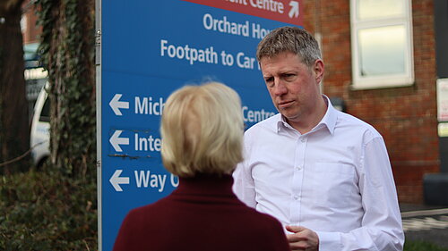 James MacCleary talking to a constituent next to an NHS signboard