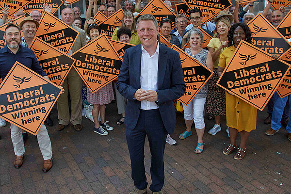 James MacCleary in front of a forest of LibDem diamond posters held by some very happy looking members